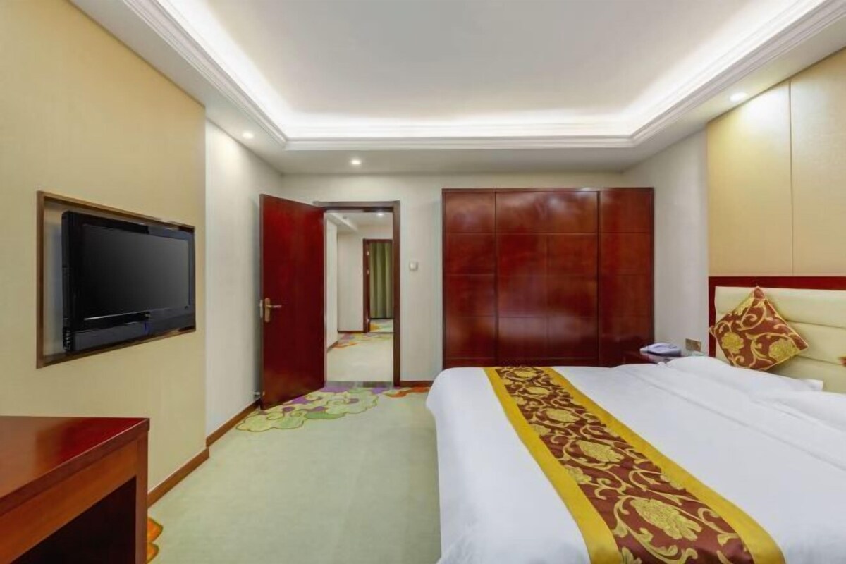 A hotel room with a bed, a TV, a wardrobe, and a door leading to another room.