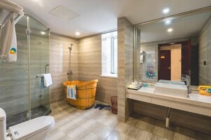 Un baño moderno con cabina de ducha de vidrio, un cubo de madera, un espejo grande y un lavabo con artículos de aseo.