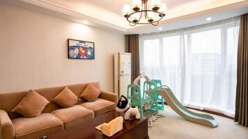A living room with a sofa, a coffee table, a chandelier, a children's slide, and a large window with curtains.