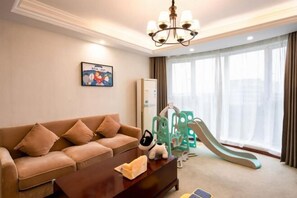 A living room with a sofa, a coffee table, a chandelier, a children's slide, and a large window with curtains.