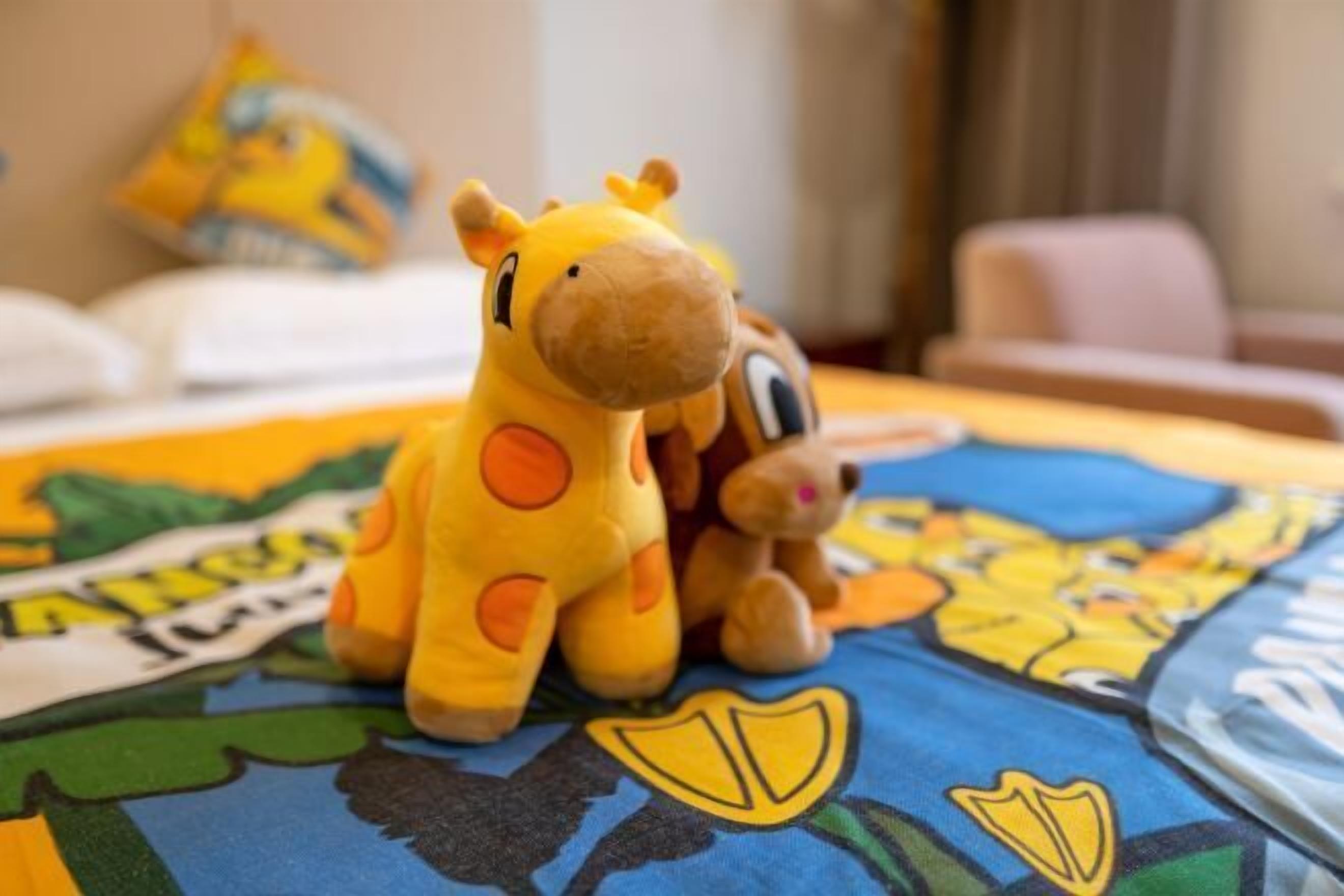 A bed with a colorful bedspread, a small stuffed giraffe, and a teddy bear.