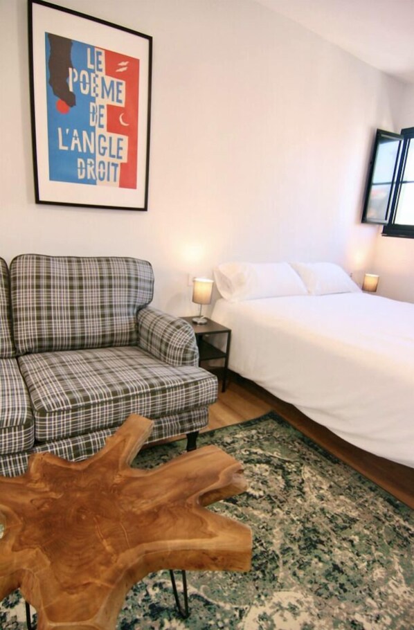 A room with a plaid sofa, a wooden coffee table, a bed with white linens, and a framed quote on the wall. - Estudio para 3 personas (Vigo)