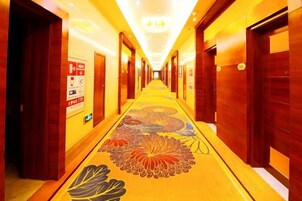 A hotel hallway with doors on both sides, a carpet with floral patterns, and a sign on the left wall.