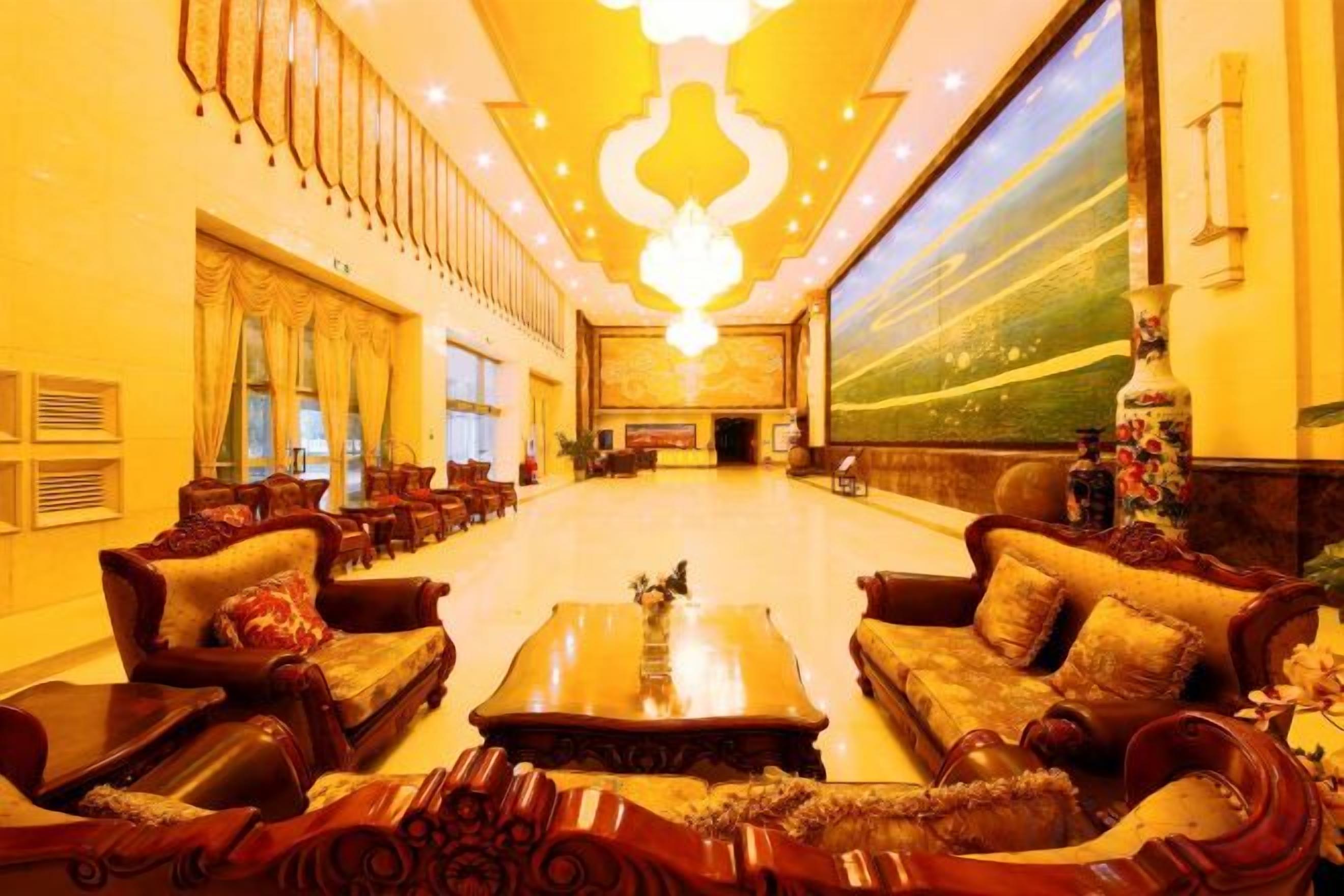 A spacious lobby with a high ceiling, ornate sofas, and a large chandelier.