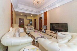 A living room with a sofa set, a coffee table, a TV, and a small table with a lamp. - Bayin Guoleng Hotel (Korla)