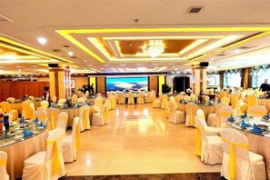 A banquet hall with round tables, white chairs, and a central stage. - Bayin Guoleng Hotel (Korla)