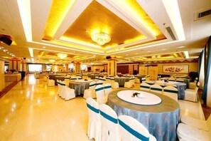 A banquet hall with round tables, chairs, and a chandelier. - Bayin Guoleng Hotel (Korla)