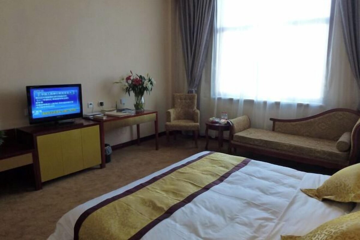 A hotel room with a bed, a television, a desk, a chair, a sofa, and a window with curtains.