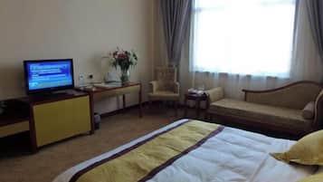 Quarto de hotel com cama, televisão, escrivaninha, cadeira, sofá e janela com cortinas.
