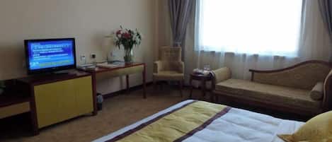 Une chambre d’hôtel équipée d’un lit, d’une télévision, d’un bureau, d’une chaise, d’un canapé et d’une fenêtre avec des rideaux.