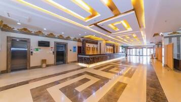 A hotel lobby with a marble floor, elevators, a reception desk, and a modern ceiling design.