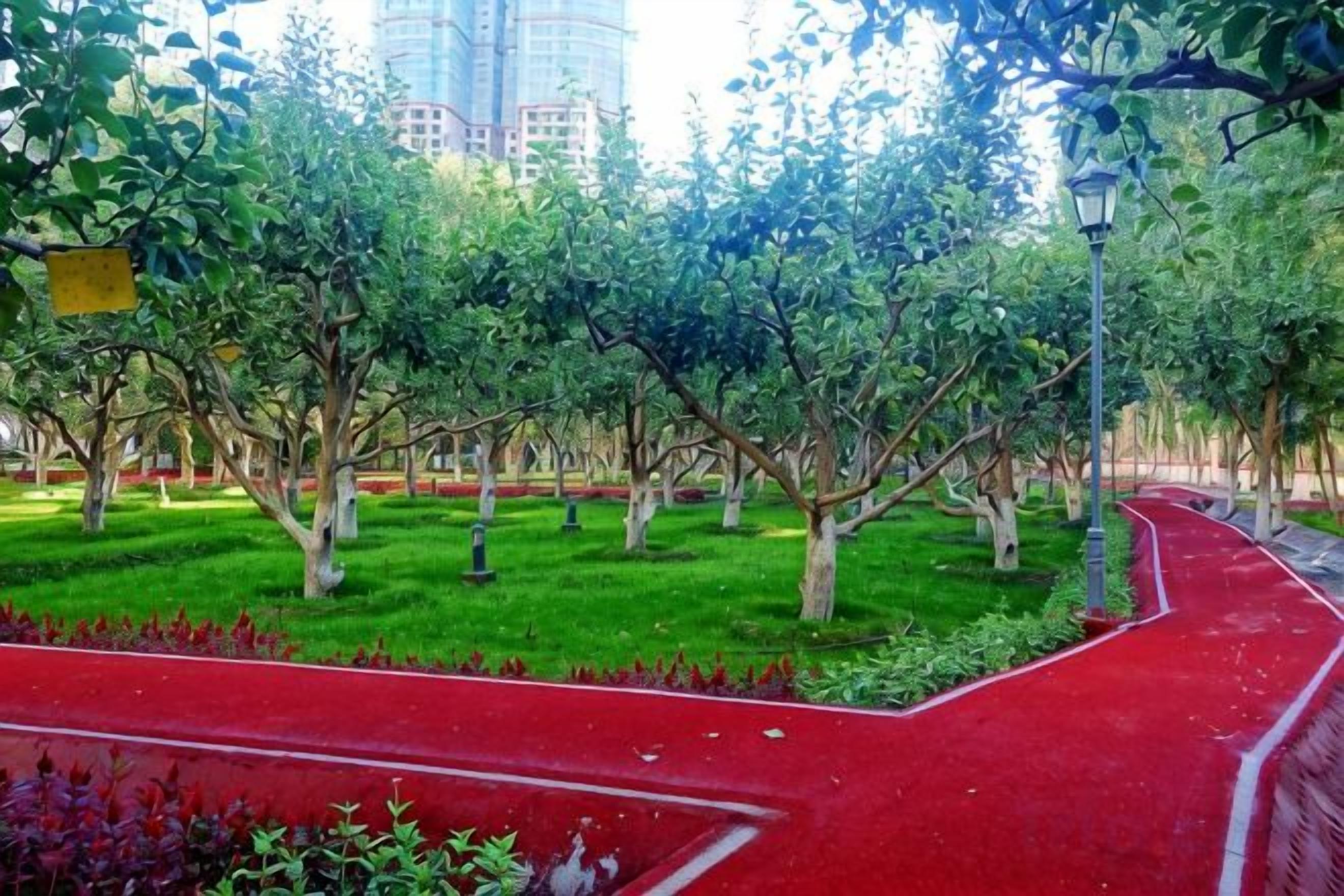 A park with a red pathway, trees, and a lamp post.