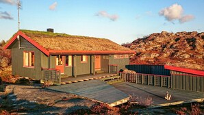 Eine kleine, rustikale Holzhütte mit einem Strohdach, einer Holzterrasse und einem eingezäunten Bereich.