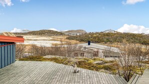 Blick von einer Gebäude-Terrasse auf eine hügelige Landschaft mit spärlicher Vegetation und einem entfernten Gewässer.
