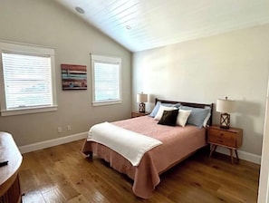 Un dormitorio con una cama, dos mesitas de noche y dos ventanas con persianas.