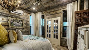 Une chambre à coucher au style rustique, avec un plafond en bois, un lit recouvert d’une couette à motifs blancs et bleus, un tableau encadré accroché au mur et une commode en bois.