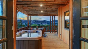 Une terrasse en bois avec un jacuzzi, des sièges d’extérieur et une vue sur un paysage montagneux.