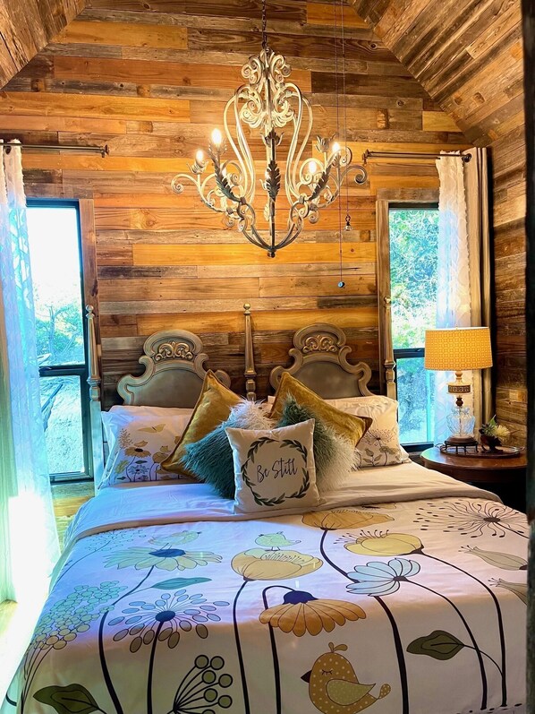Ein Schlafzimmer mit Holzboden, einer Kristallleuchtre, einem Bett mit Blumenmuster und einem Nachttisch mit Lampe.