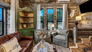 Un intérieur rustique avec un canapé en cuir, une étagère verte, un lustre et une tête de cerf accrochée au mur.