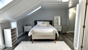 Un dormitorio con cama, mesitas de noche, cómoda, espejo y ventana.
