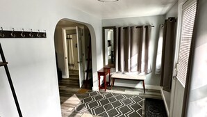 Un pasillo con un banco, un perchero y una puerta que da a otra habitación.