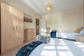 Cozy retreat with a large bed, wardrobe, and nightstand, plus a door to another room and a chair for relaxation.
