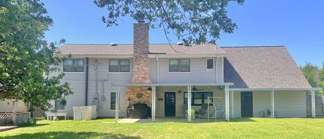 A two-story house with a brick chimney, a covered patio with outdoor furniture, and a well-maintained lawn.