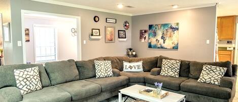 A living room with a sectional sofa, a coffee table, and various wall decorations including a clock and framed pictures.