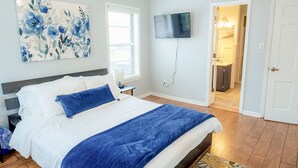 A bedroom with a bed, a TV mounted on the wall, and a door leading to a bathroom. - Luxe 5BR Family Retreat, Minutes From TAMU (College Station)