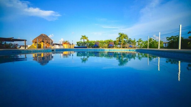 A clear blue pool with a reflection of palm trees and a thatched-roof building. - Encanto Riviera (Playa del Carmen)