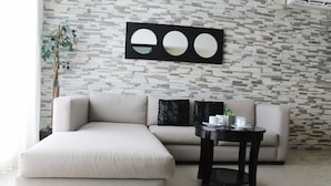 A modern living room with a sectional sofa, a round coffee table, and a decorative wall with a geometric pattern. - Encanto Riviera (Playa del Carmen)