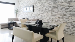A modern dining area with a glass table, four chairs, and a stone wall backdrop. - Encanto Riviera (Playa del Carmen)