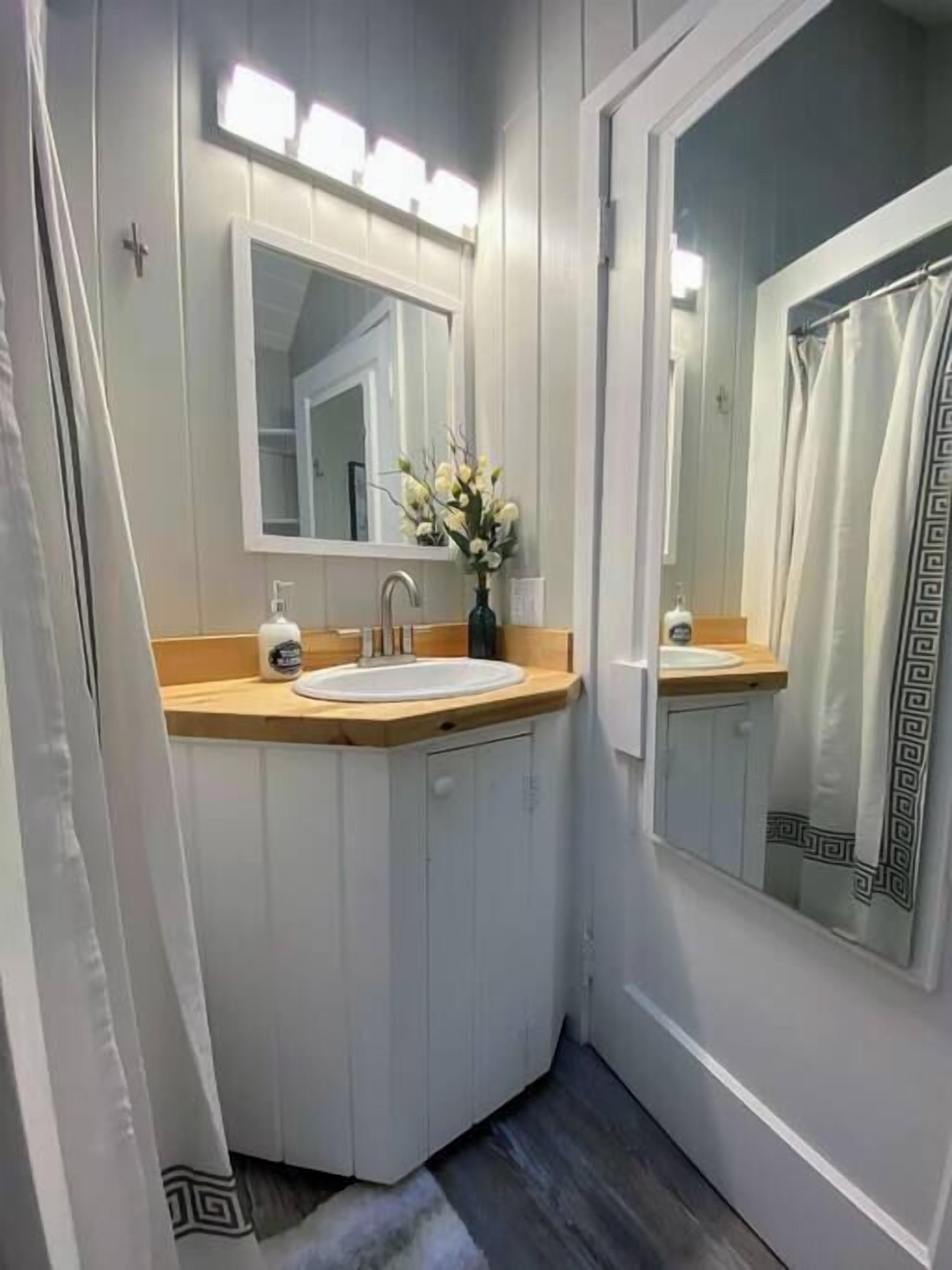 A bathroom with two sinks, a mirror, a vase with flowers, and a shower curtain with a geometric pattern.