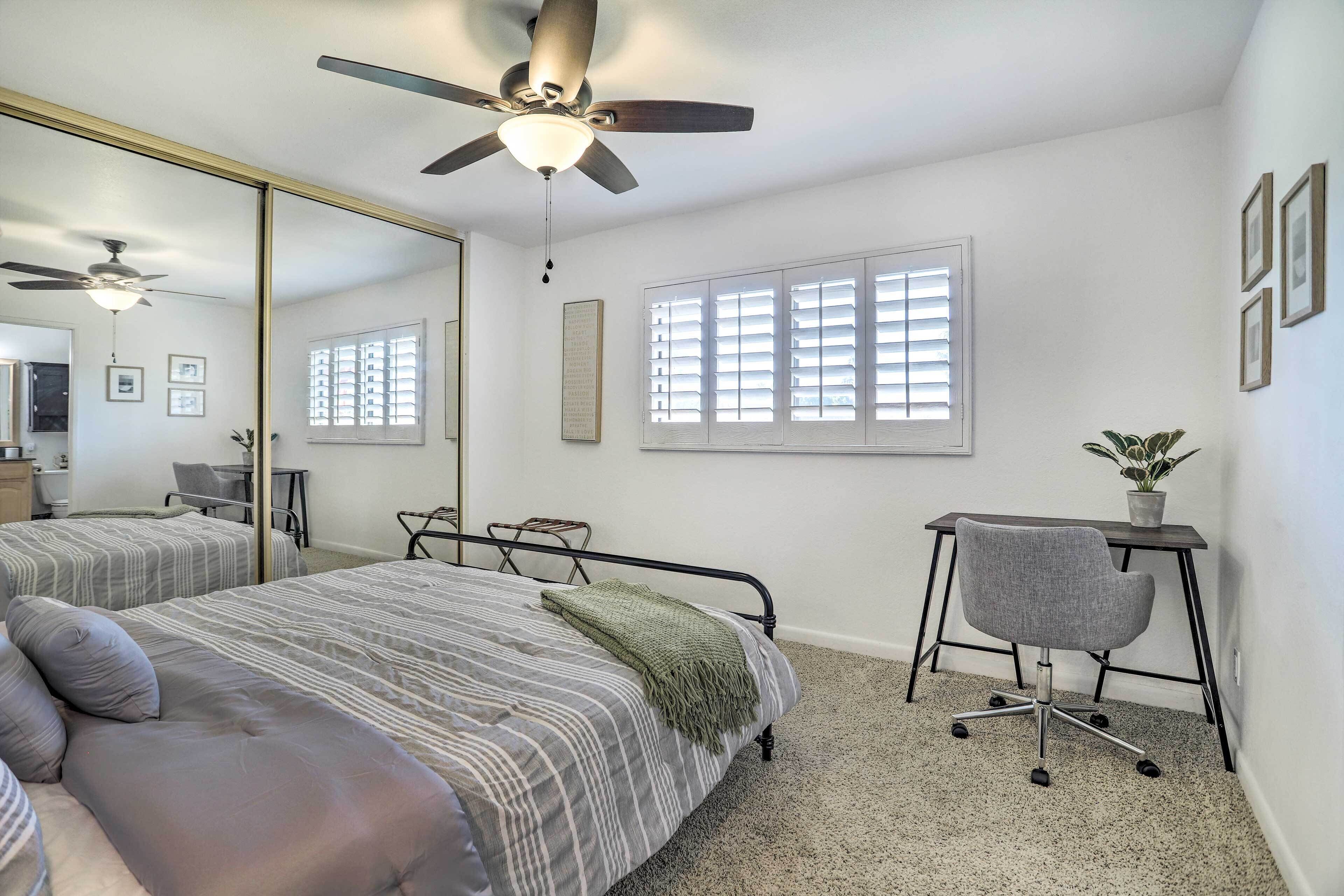 A bedroom with a bed, a desk, a chair, a ceiling fan, and a window with blinds.