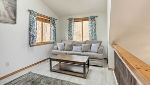 Uma sala de estar com um sofá, uma mesa de centro e duas janelas com cortinas.