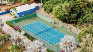 Ein Tennisplatz, umgeben von viel Grün und einem blauen Gebäude.