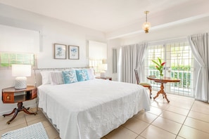 Une chambre d’hôtel avec un grand lit, deux tables de chevet, une petite table ronde, un balcon avec vue et un luminaire au plafond.