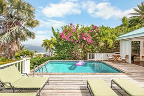 Una piscina con sillones de descanso, rodeada de exuberante vegetación y vistas al océano.