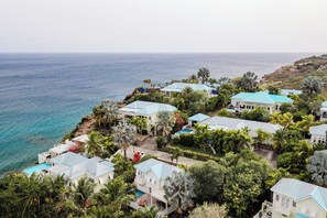 Un quartier résidentiel situé sur la côte, avec des maisons aux toits bleus, entouré d’une végétation luxuriante et offrant une vue sur la mer.