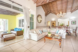 A spacious living room with a white sofa, a glass coffee table, and a dining area with wooden chairs.