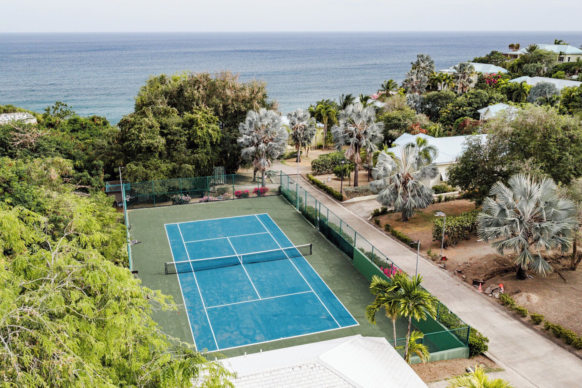 A tennis court with a net, surrounded by greenery and a view of the ocean.