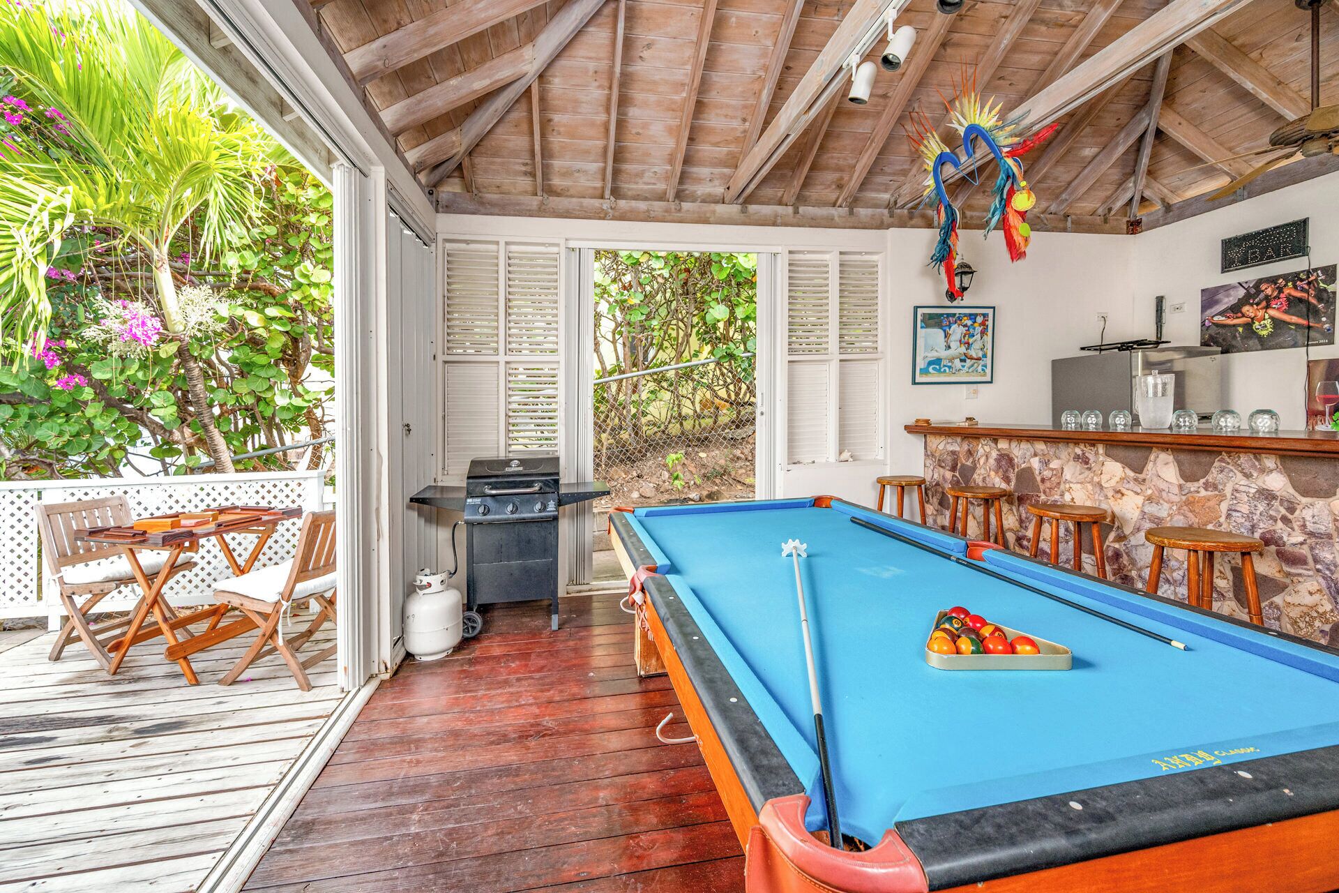 A pool table with a pool cue, a grill, and a bar area with stools.