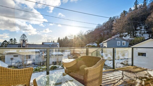 A glass-enclosed balcony with wicker furniture and a view of a snowy landscape and houses.