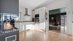 A modern kitchen with white cabinets, a built-in oven, and a large window overlooking a snowy landscape.