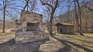 Une construction en pierre dotée d’une cheminée, entourée d’arbres et d’une petite cabane en bois.
