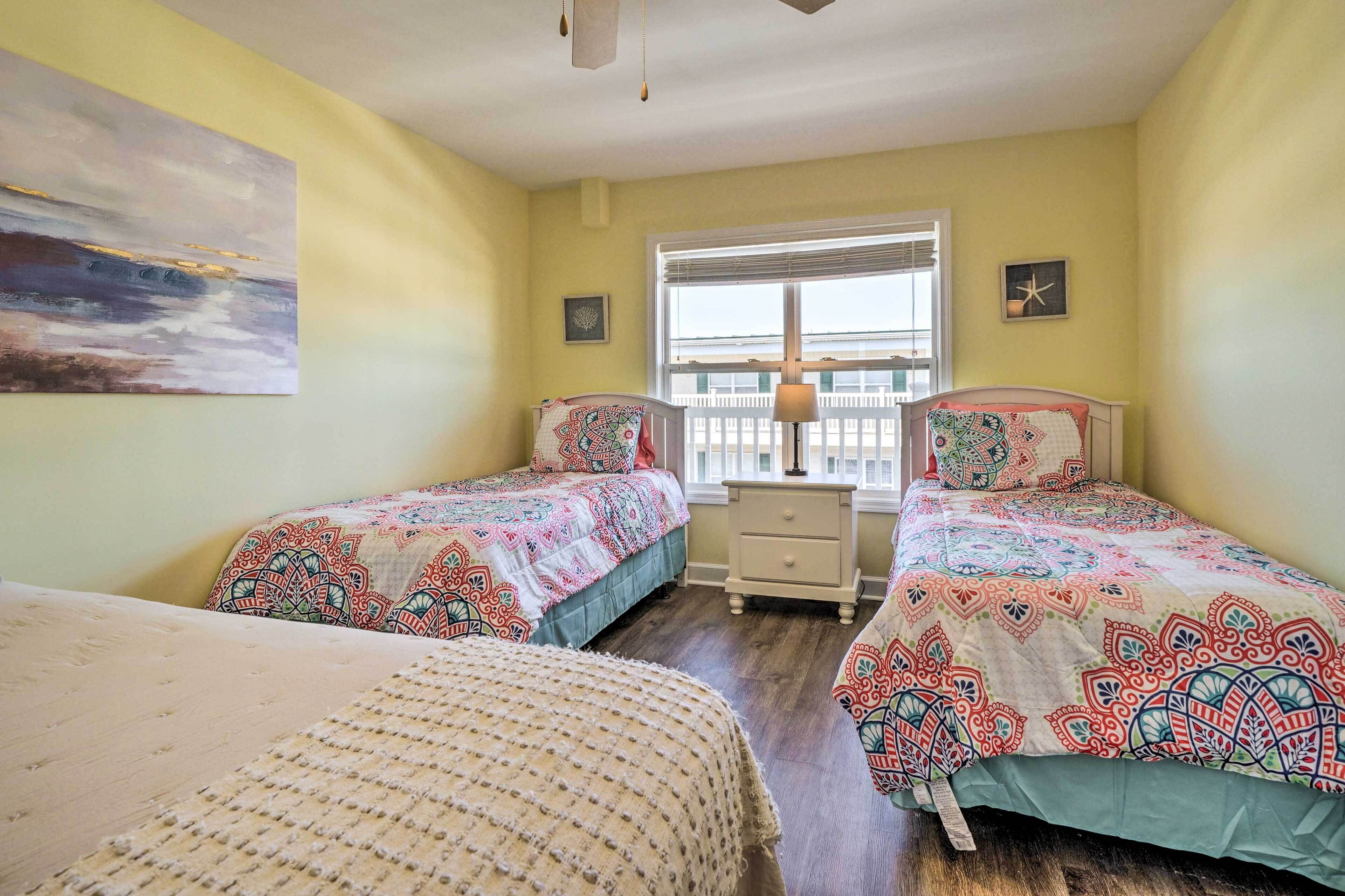A bedroom with two beds, a window with blinds, a nightstand, and a painting on the wall.