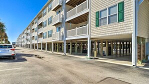 A multi-story building with balconies, a covered parking area, and a clear sky. - Oak Island Condo - Walk to the Beach! (Oak Island)