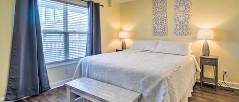 A bedroom with a bed, a bench, two bedside lamps, a ceiling fan, and decorative wall art.