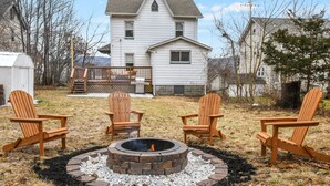Un patio trasero con un brasero y cuatro sillas Adirondack.