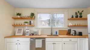 Una cocina con armarios blancos, encimeras de madera, una ventana y diversos utensilios de cocina.